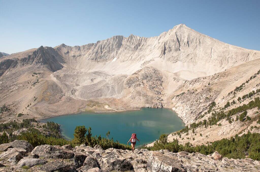 female backpacker with large backpack with blue alpine lake and rugged mountains in background