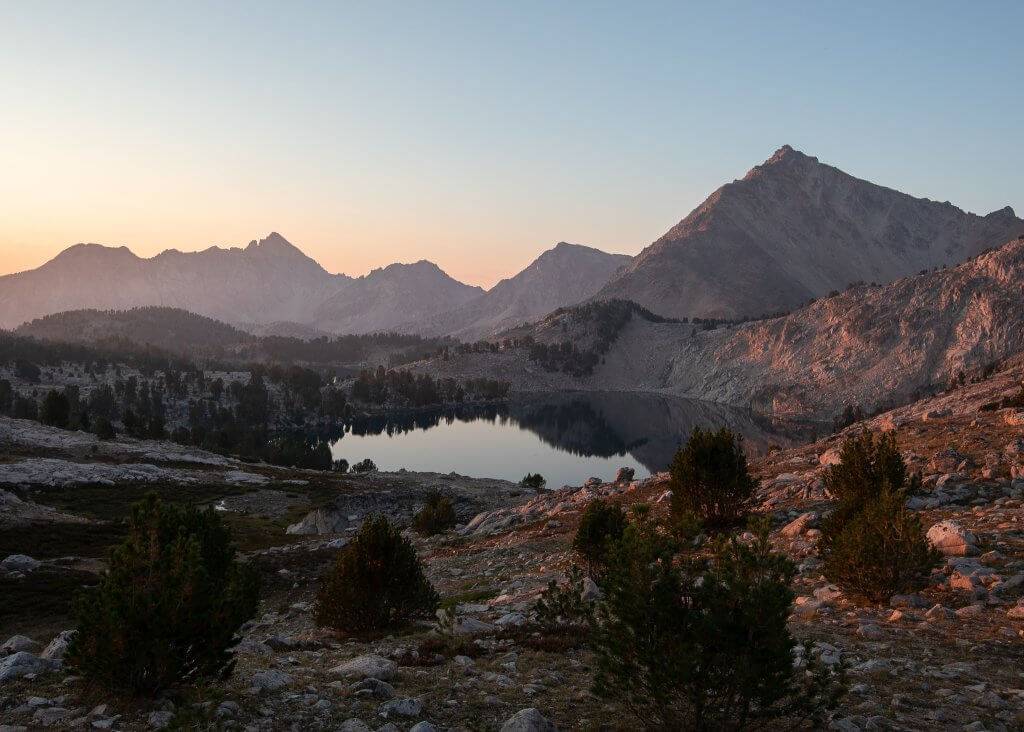 alpine lake at sunset reflecting purple hues with rugged mountains in background