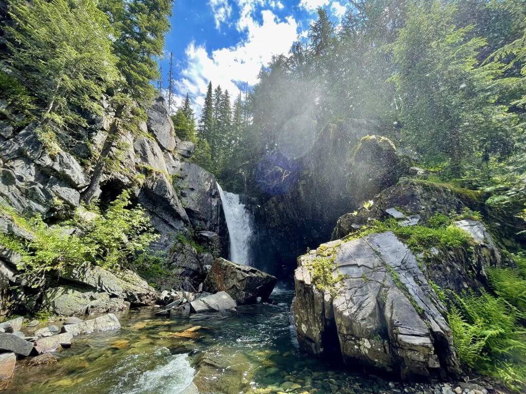 Char Falls tumbles down rocky canyon with blue skies and trees surrounding it