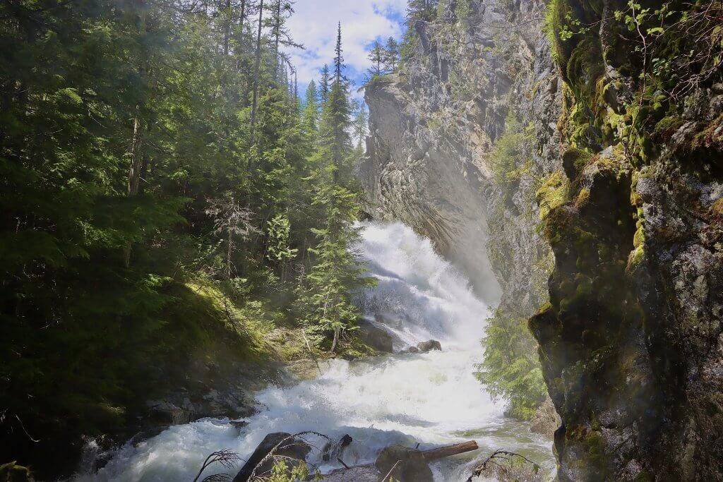 wide image of Granite Falls in steep canyon with tall trees surrounding water