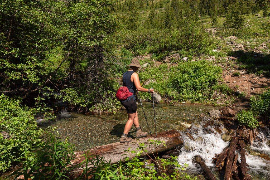 woman crossing a creek by walking across a log laying across the creek