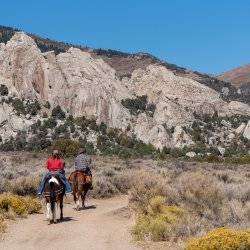 Two horseback riders on dirt trail riding away with rock formations in the distance at Castle Rocks State Park.