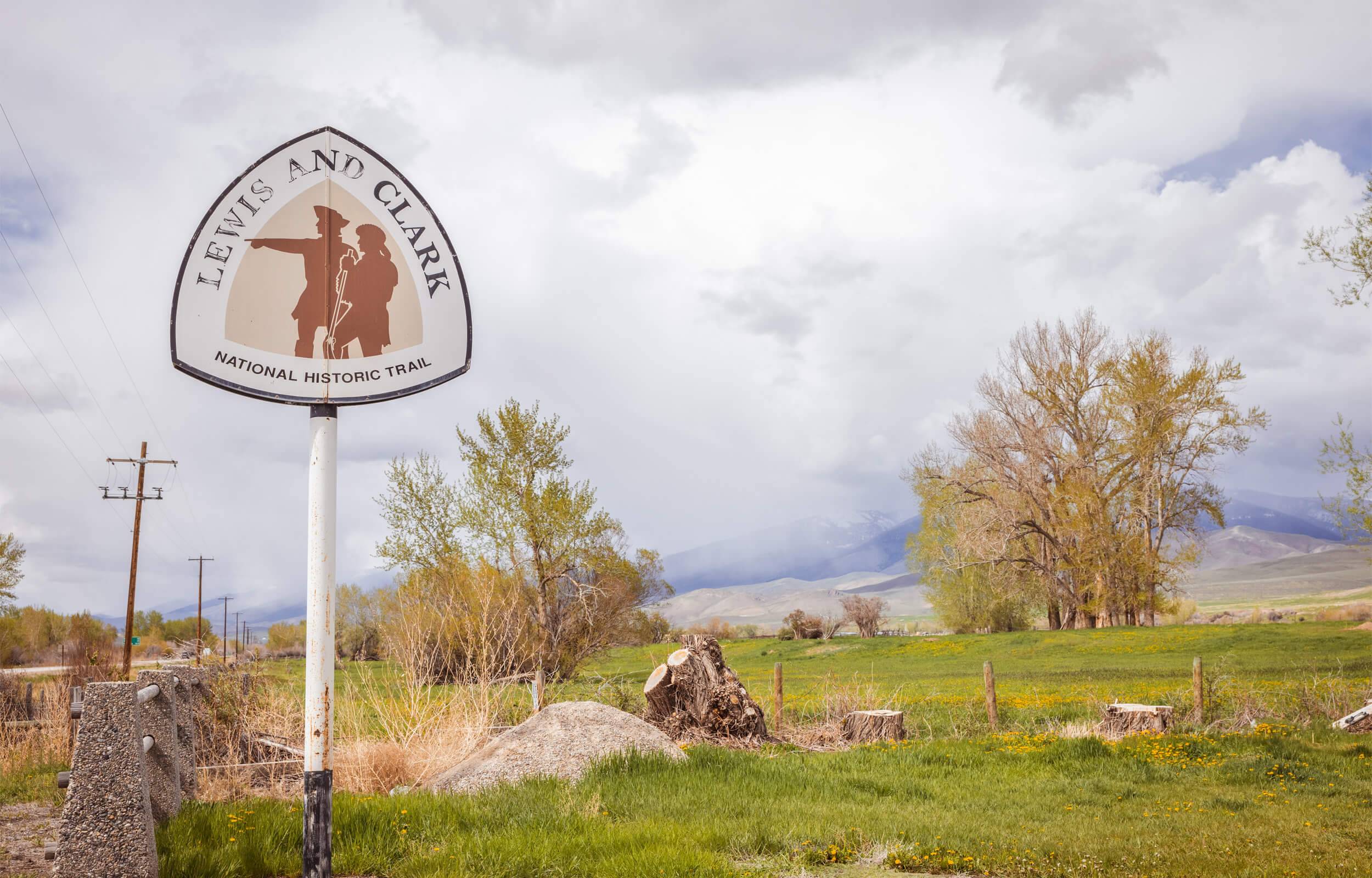 View of the Lewis and Clark National Historic Trail sign in a grassy field with trees scattered around.