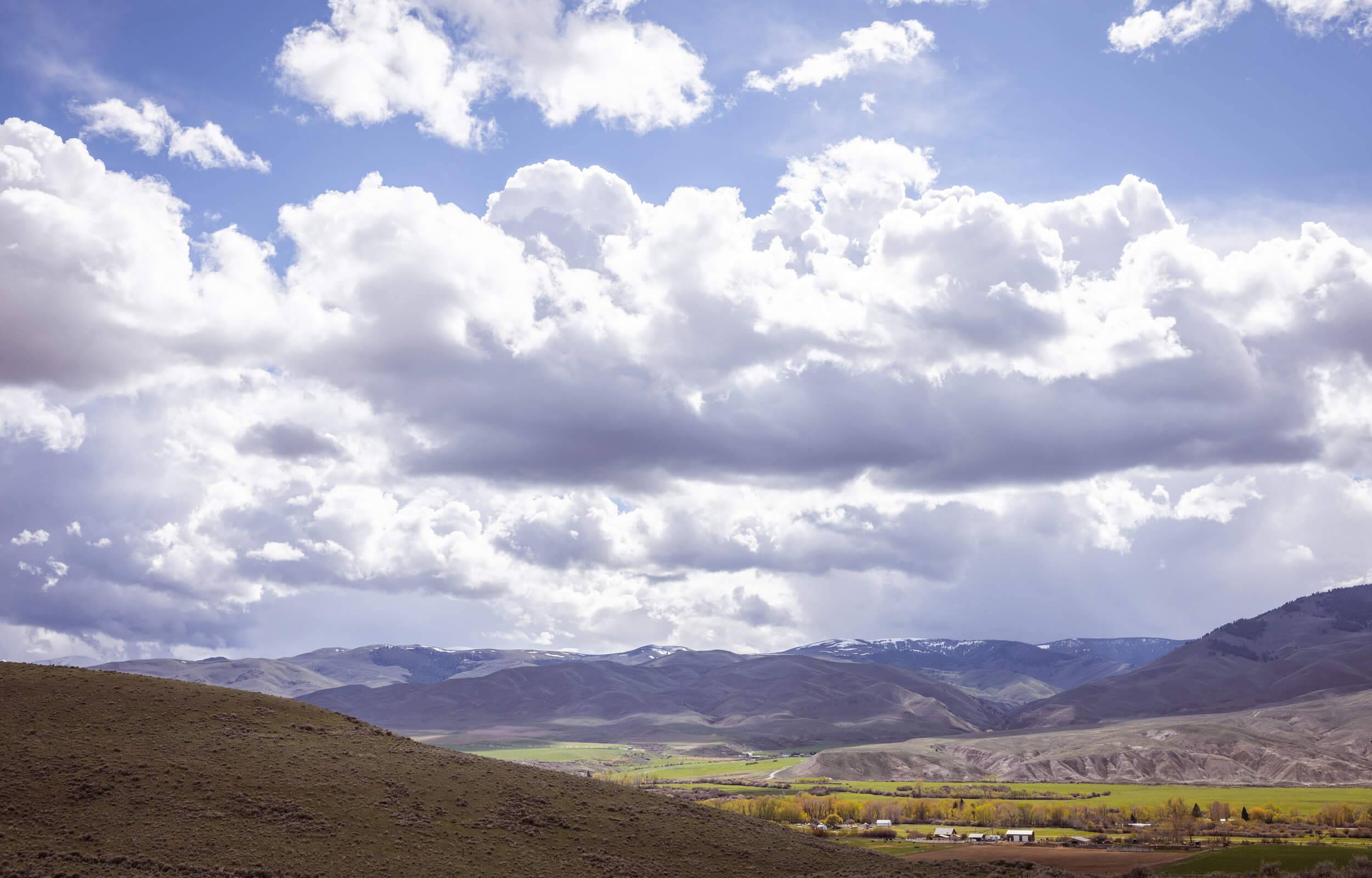 View of an open landscape with trees and a few buildings, and mountains in the distance.