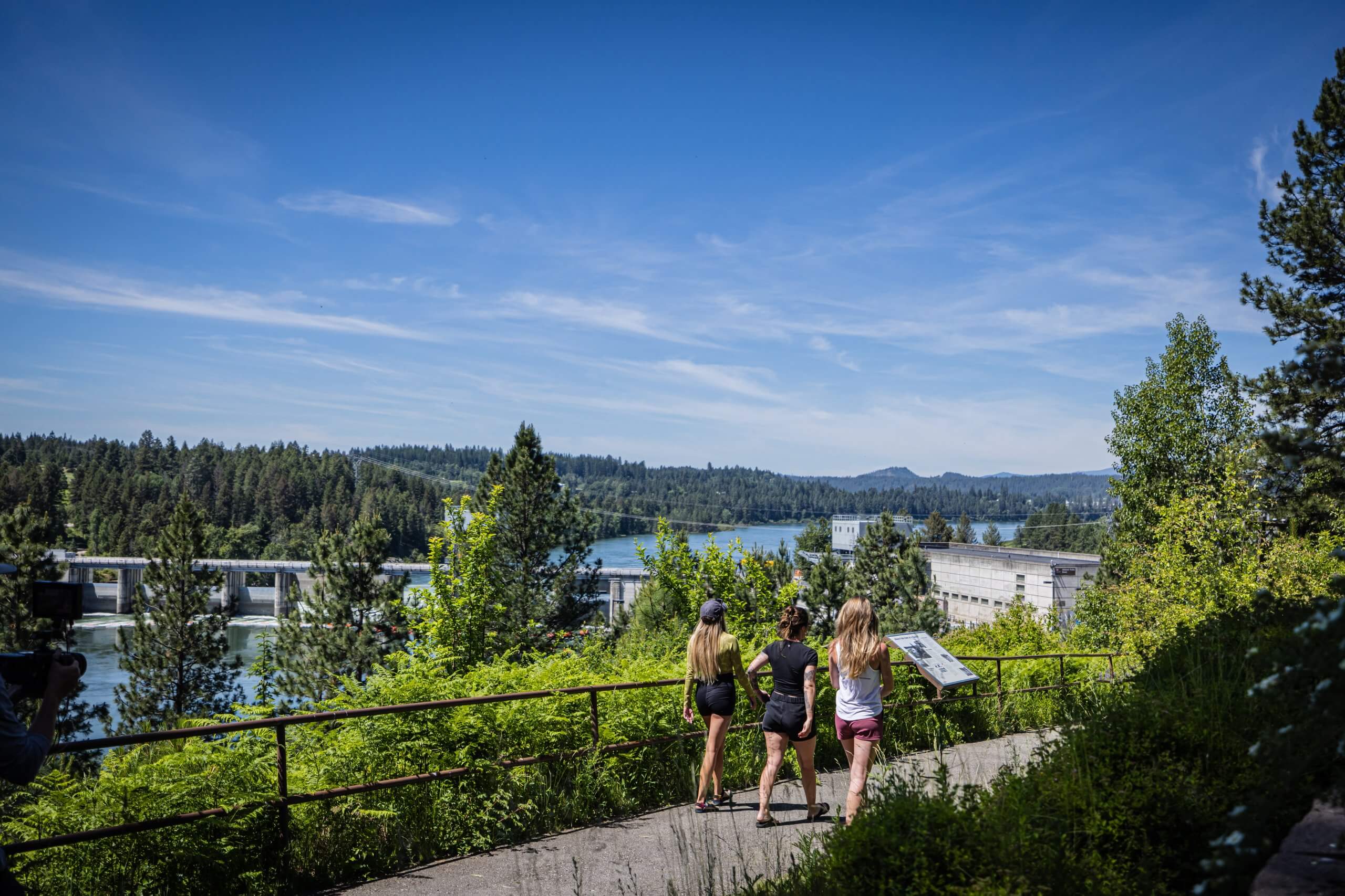 three women walk along a pathway overlooking a river.