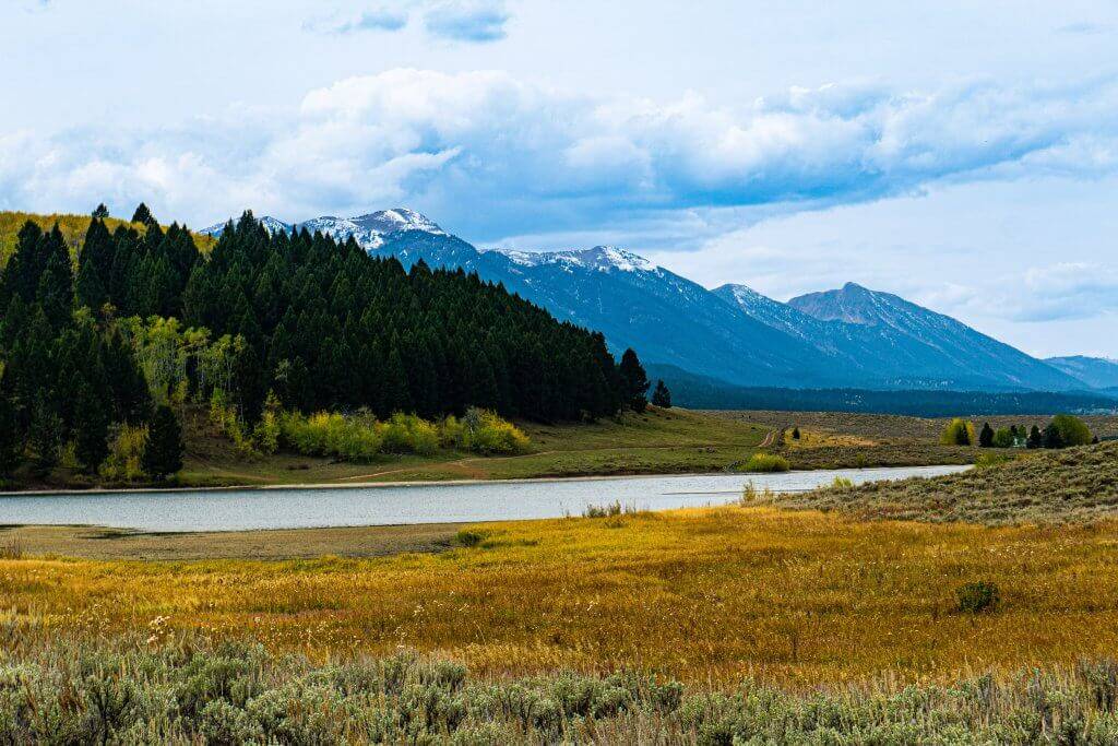 wide shot of lake surrounded by short grasses with mountains in the background