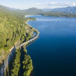 An aerial view of the Pend Oreille Scenic Byway winding between a forest and Lake Pend Oreille.