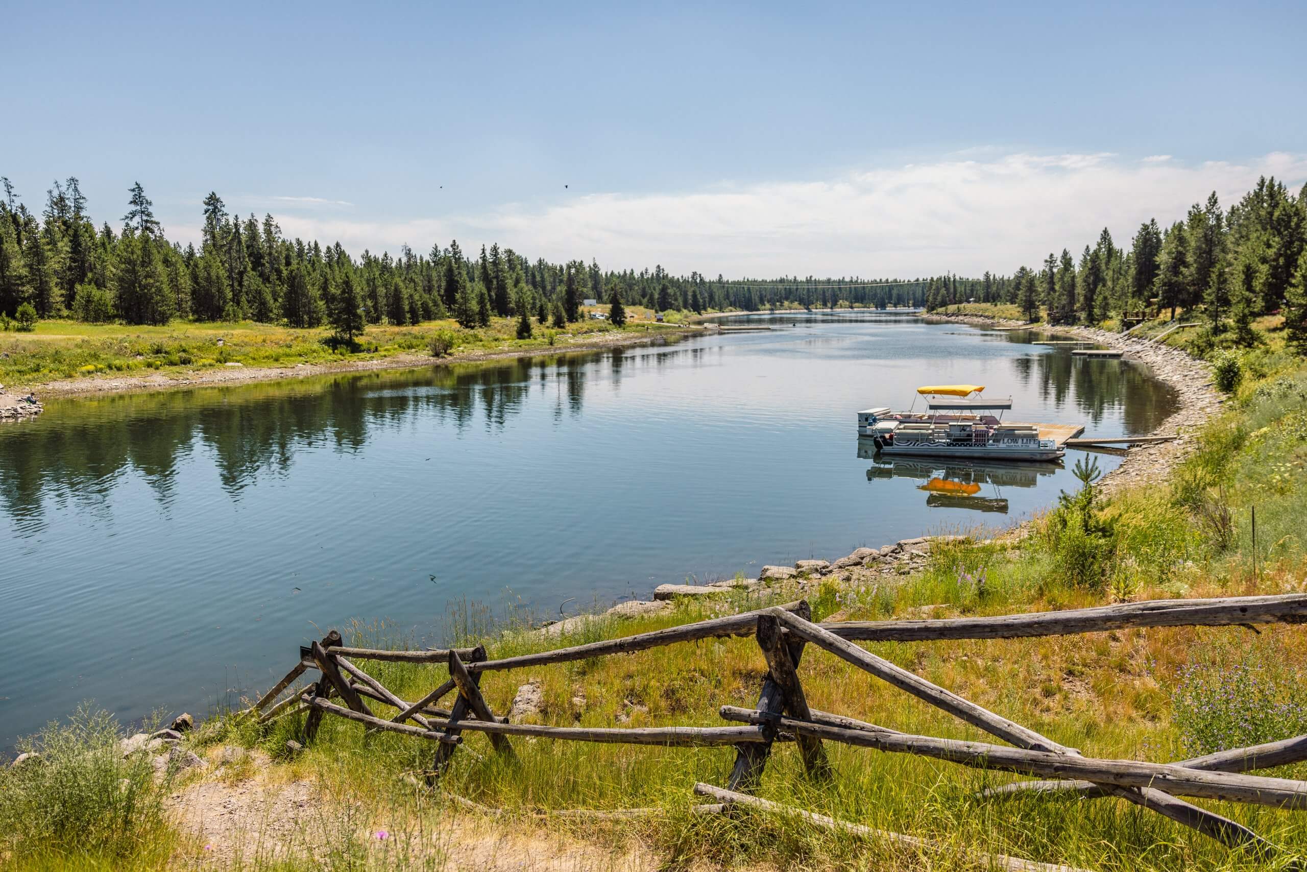 view of the tree-lined henrys fork of the snake river, with a boat on the riverbank.