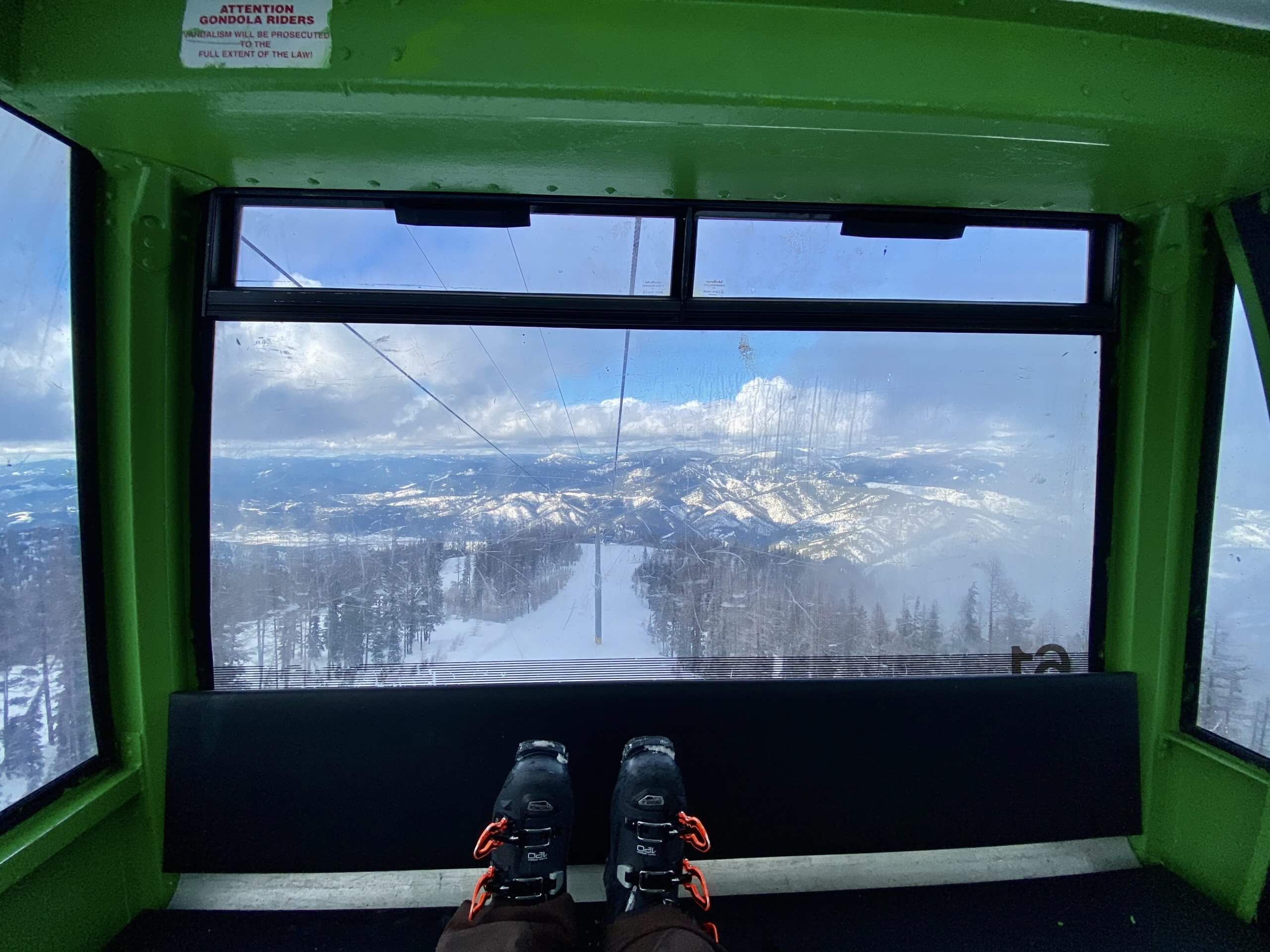 interior of green gondola at silver mountain, showing ski boots resting on seat with views of the snowy Silver Valley out of the window
