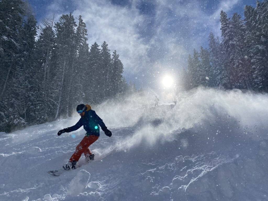 snowboarder at Lookout Pass coming down snowy hill with large glowing sun in background