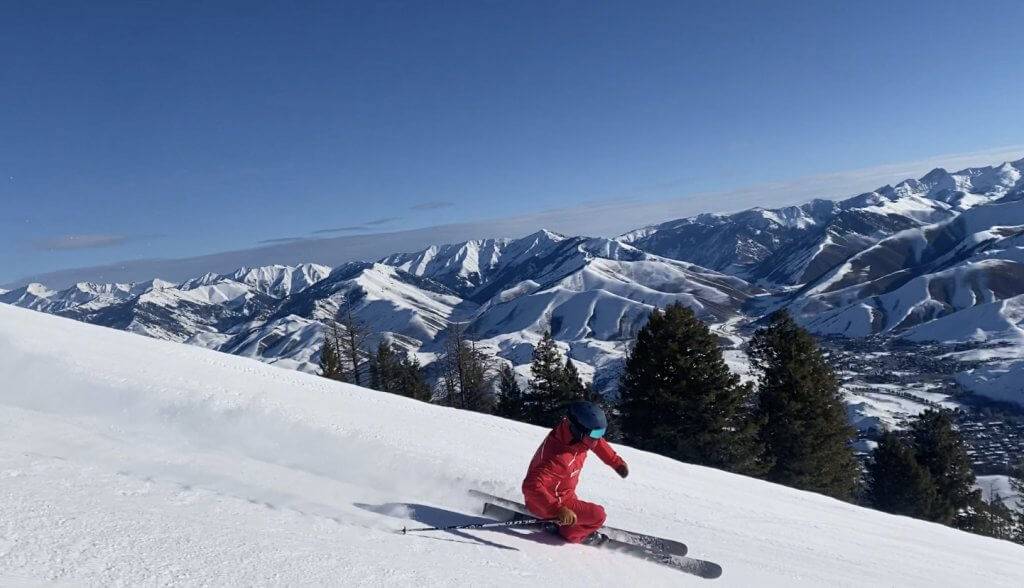 downhill skier in red jacket skiing down snowy mountain with other snowy mountains in the background