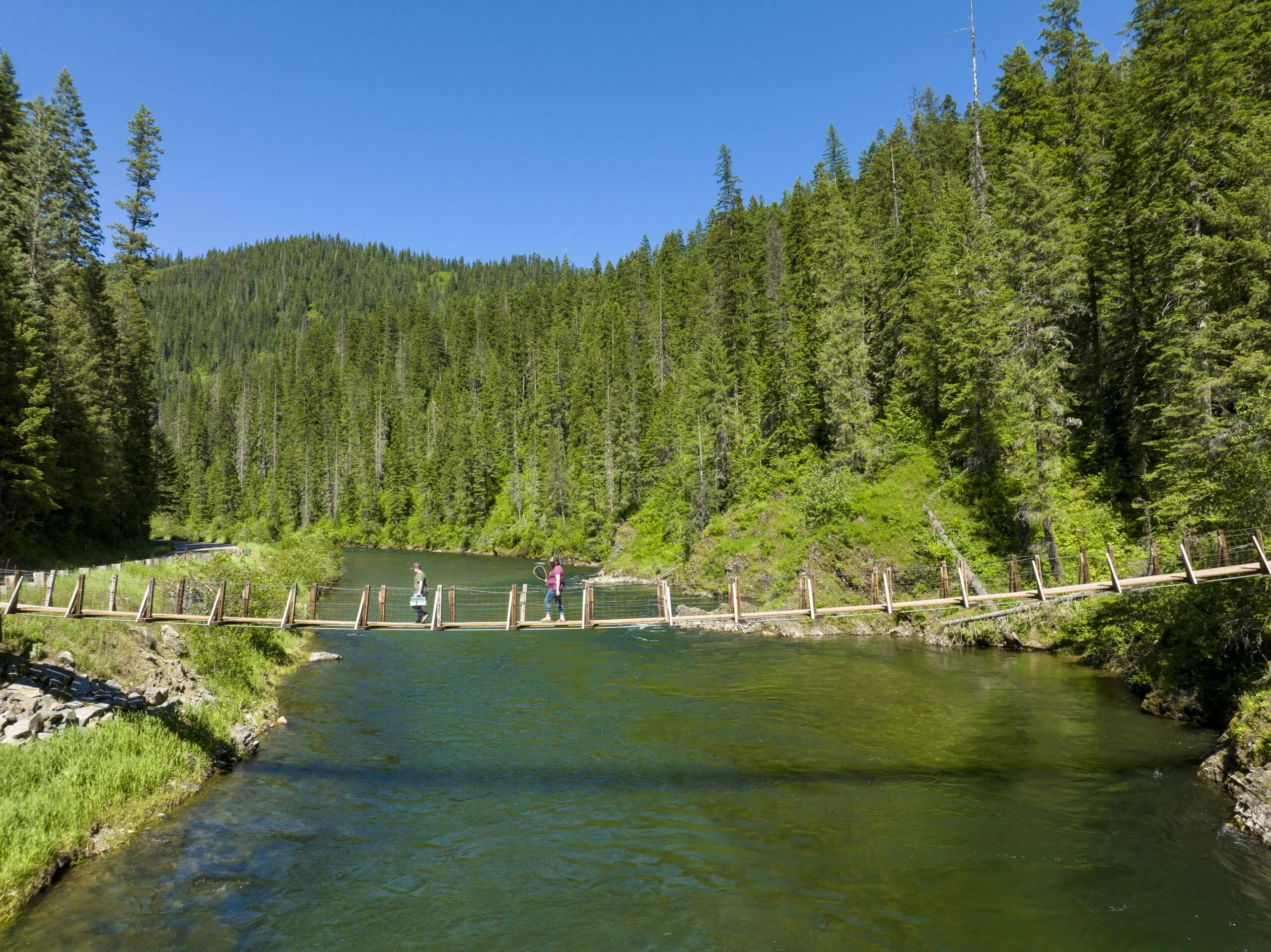 Two people walk across a wooden suspension bridge.