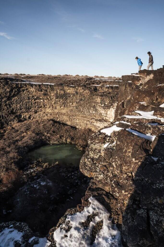 mom and son in winter coats looking over canyon edge at blue water pools below