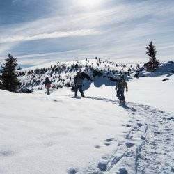 thee people in heavy winter coats are snowshoeing in a line on top of a snowy path at craters of the moon