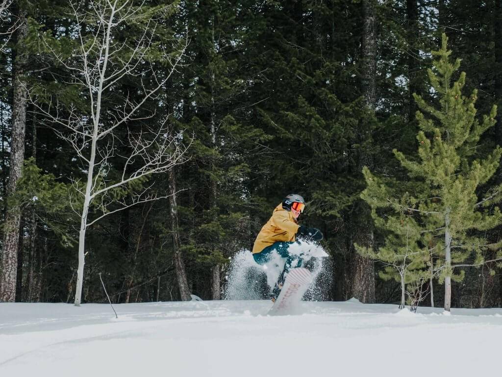 a snowboarder coming out of the trees down a snowy hill