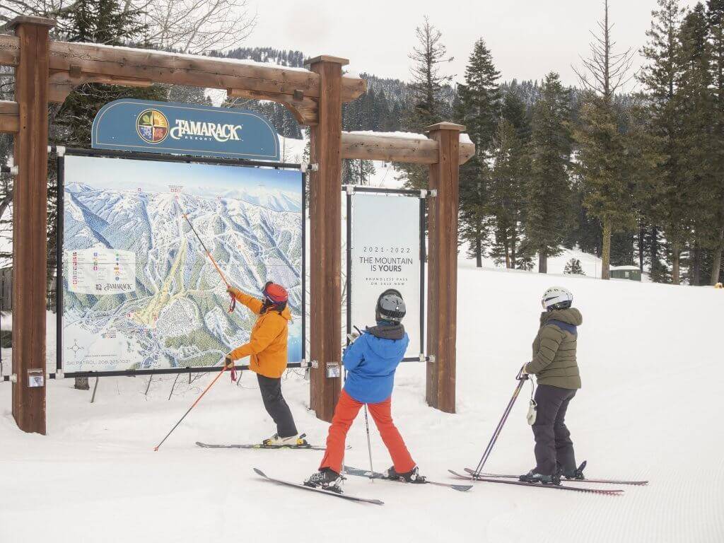 three skiers standing in front of very large ski run map for Tamarack Resort