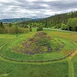 An aerial view of the Heart of the Monster site, surrounded by a sprawling field and a tree-covered hill off the side.