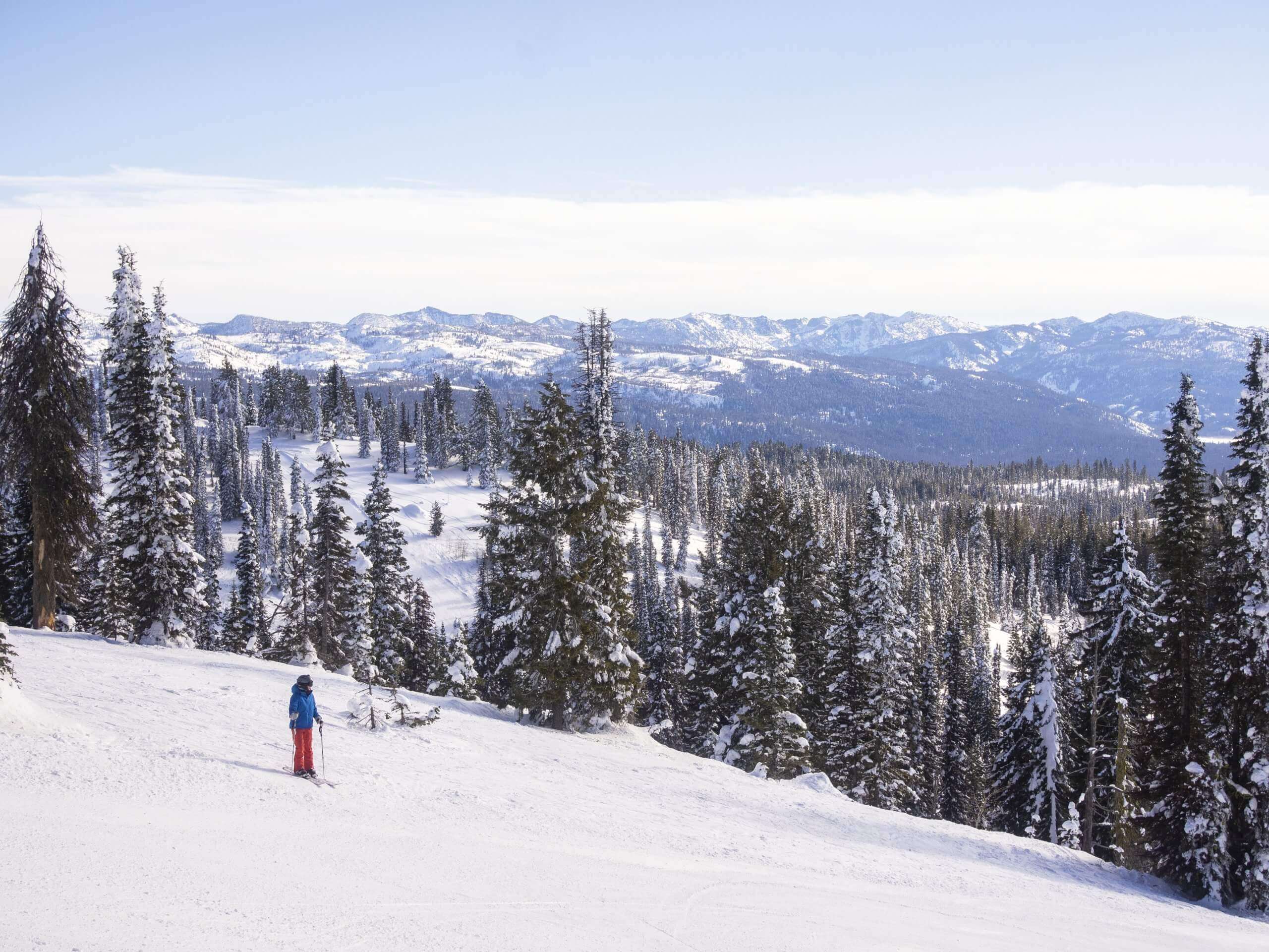 A person stopped on ski run looking out over snowy valley filled with trees at Brundage Mountain Resort.