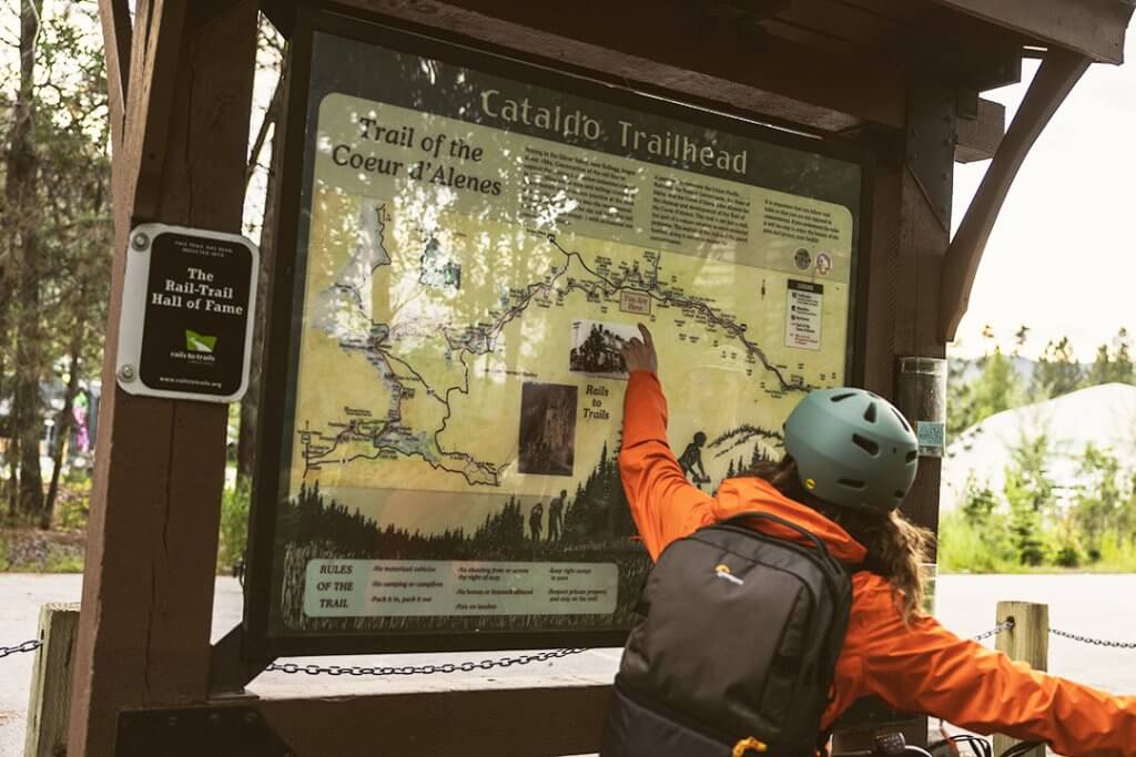 A person points at a map of the Trail of the Coeur d’Alenes at the Cataldo Trailhead.