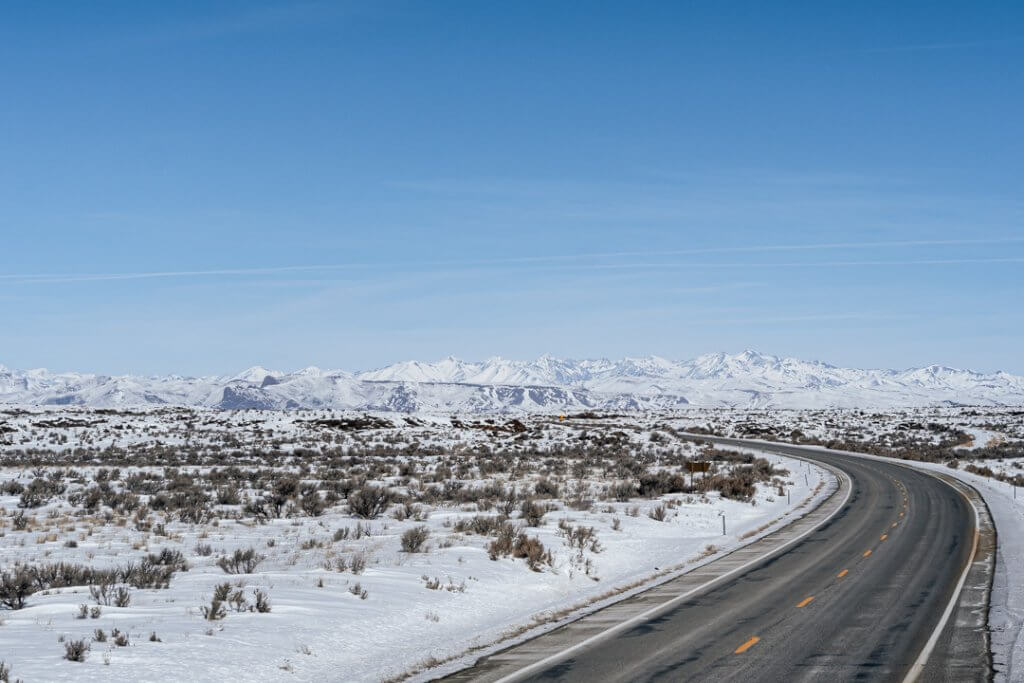 a snow-dusted road to craters of the moon with jagged rock formations on both sides of the road covered in snow under a blue sky