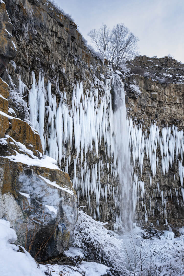 a mom and son standing, looking up at frozen waterfall