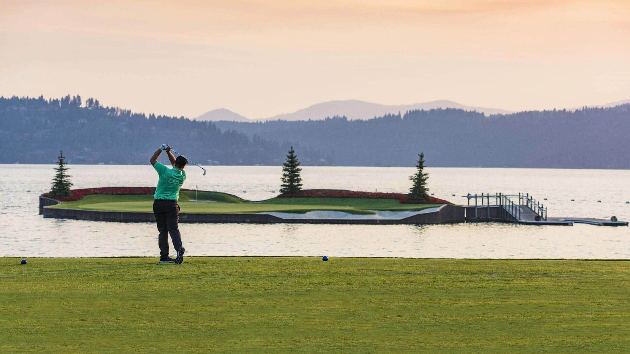 A man swings a golf club on a course near a lake.