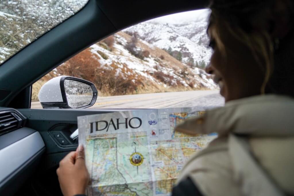 a black woman sitting inside of a car looking at and holding a road map of Idaho