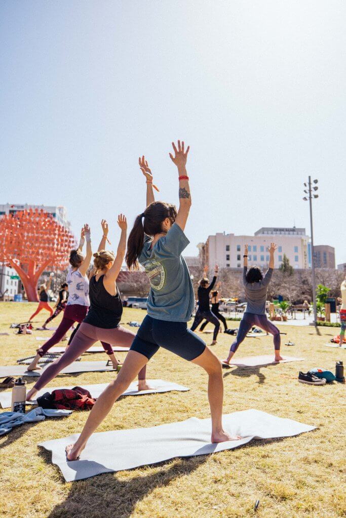 Five people in athletic attire stand on yoga mats in the grass at Yogafort in downtown Boise. 