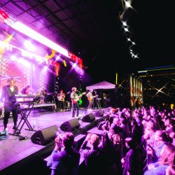 Main Stage at Treefort Music Fest light up by neon purple lights. A guitarist and keyboard player are on stage with a large crowd of people gathering at the bottom of the elevated stage.