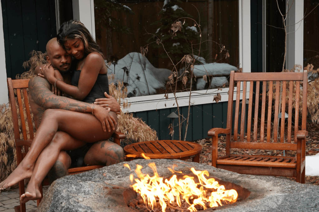 a black man and woman sitting next to a fire pit in their swimsuits at The Cove spa