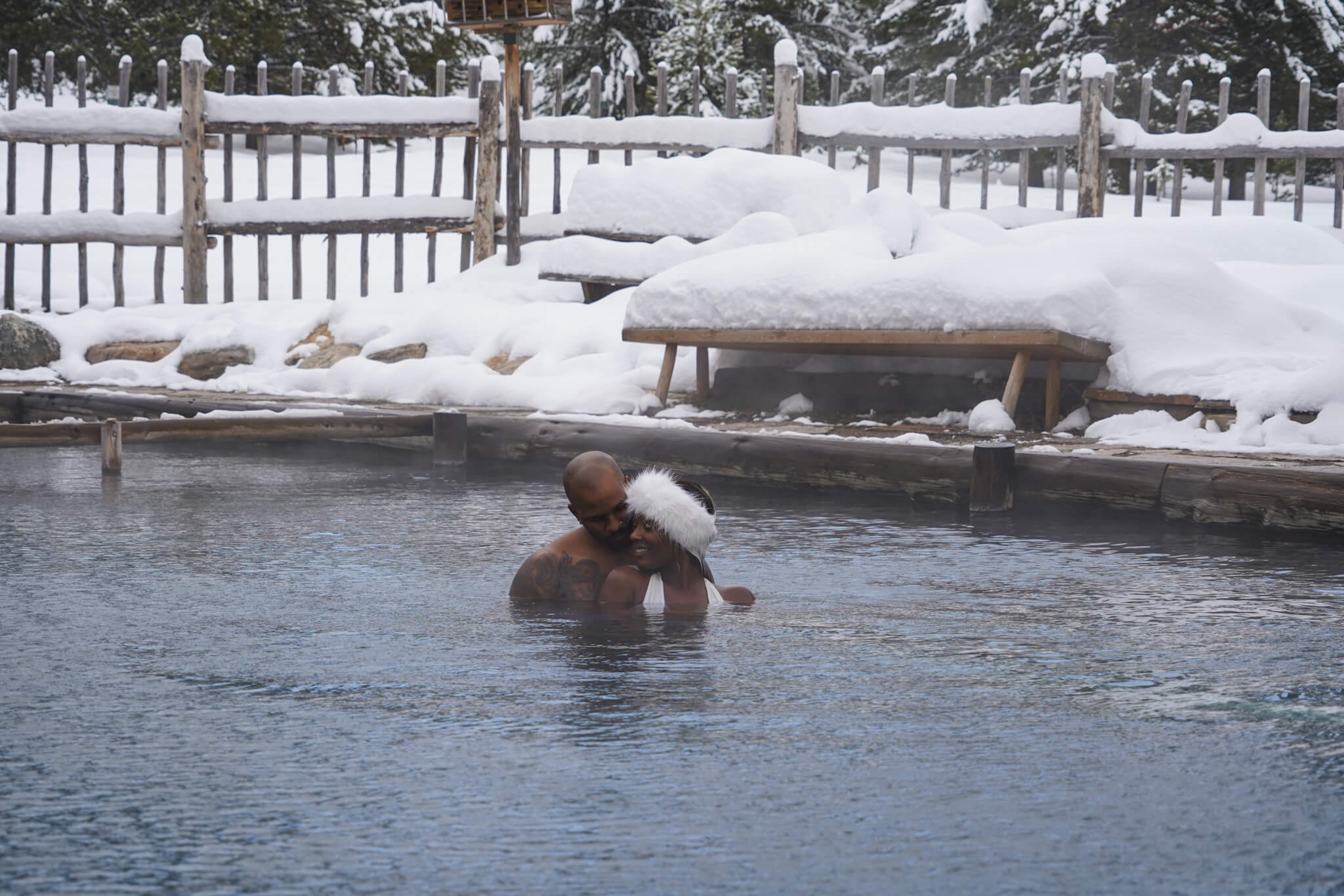 two black people soaking in a natural hot springs surrounded by snow at Burgdorf hot springs.