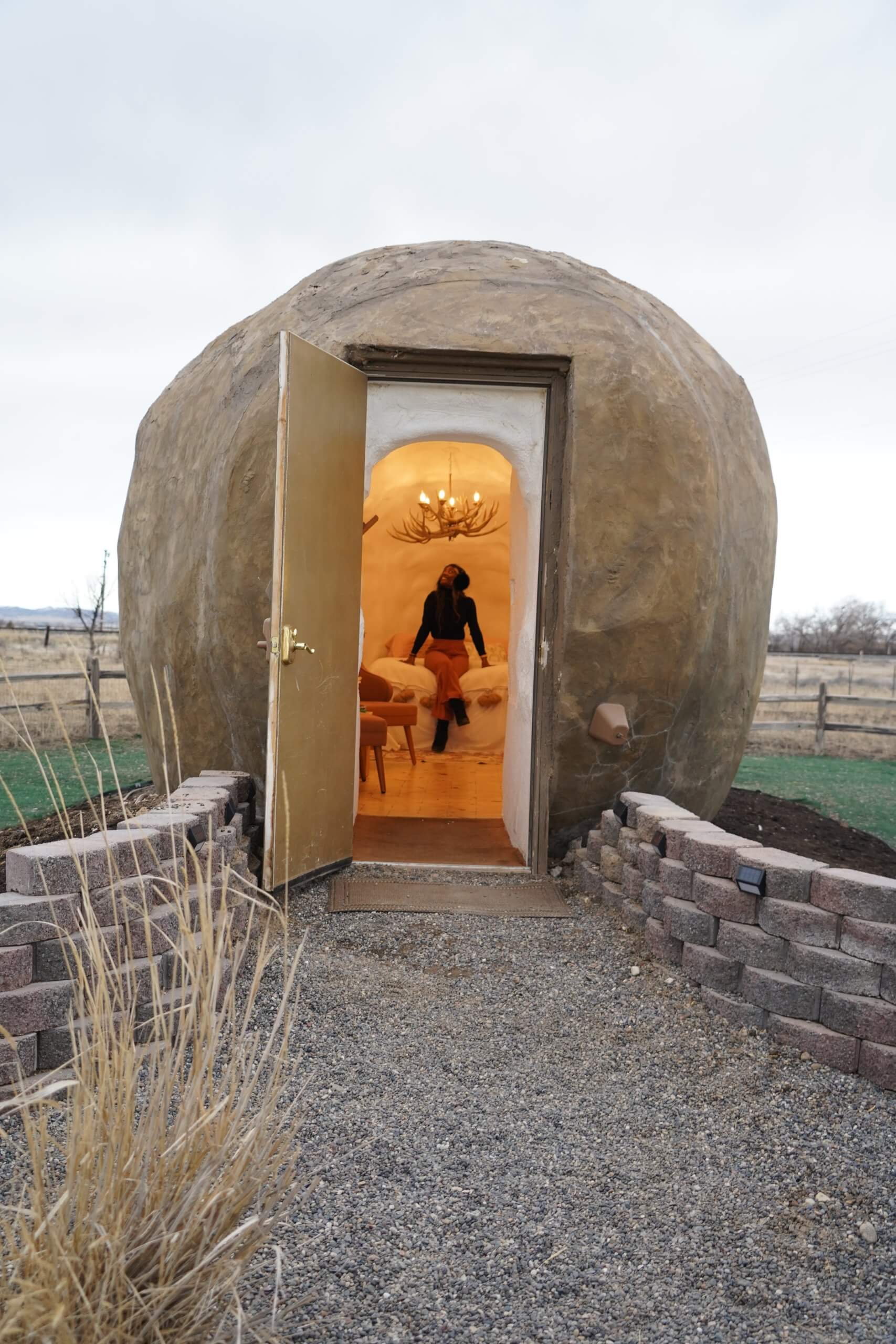 a woman sits on a bed inside a giant potato with an antler chandelier above her head at the Big Potato Hotel