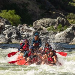 A whitewater raft with seven people dropping into a splashy rapid on the Snake River in Hells Canyon.