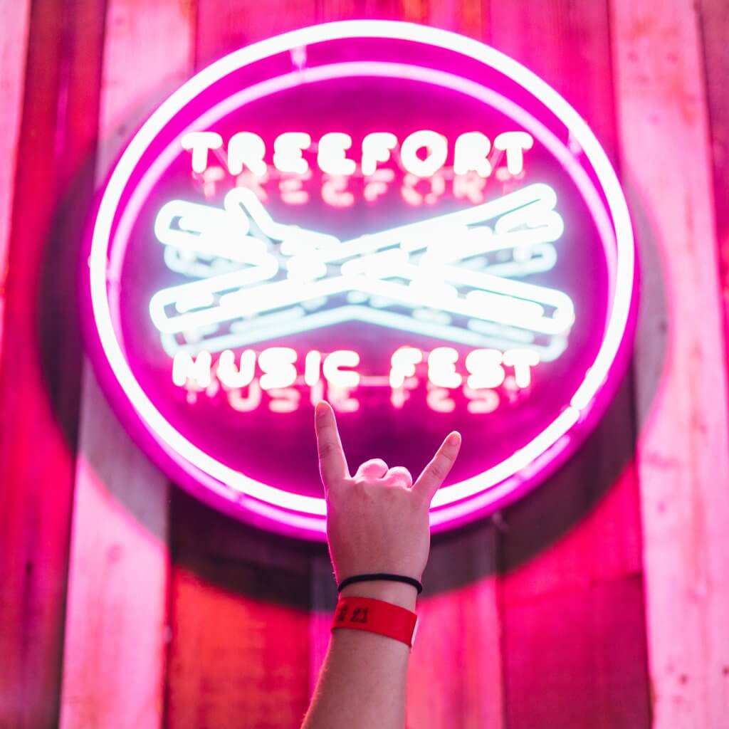 A person holds up their hand in front of a neon pink and white Treefort Music Fest sign.