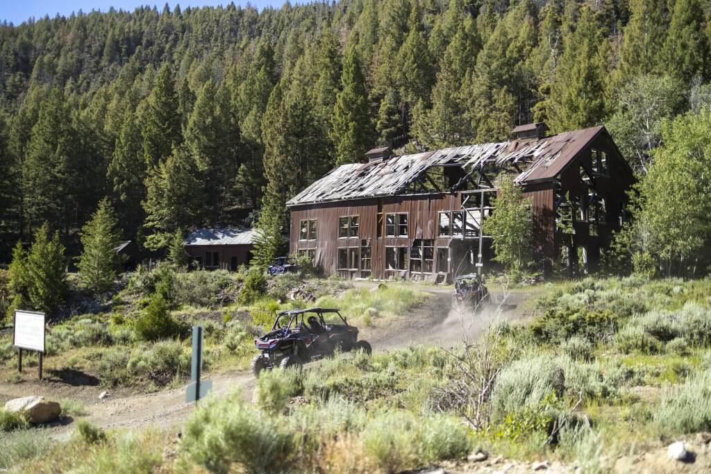 An ATV climbs up a dirt hill and approaches an old building at the Mackay Mine Hill Tour.