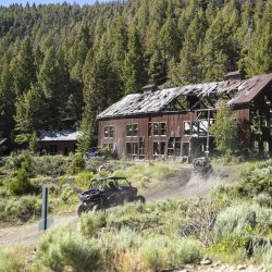 An ATV climbs up a dirt hill and approaches an old building at the Mackay Mine Hill Tour.