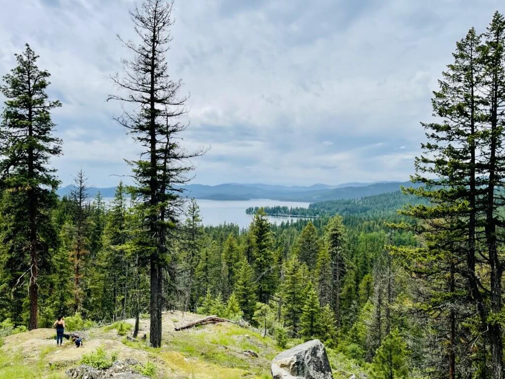 A mother and son stand on a rocky outcropping overlooking the vast Priest Lake from an scenic overlook.