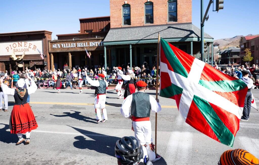 People in traditional Basque clothing wave flags while walking in a parade.