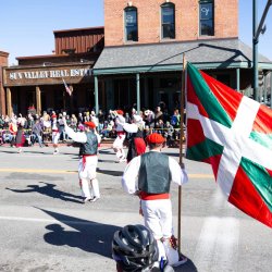 People in traditional Basque clothing wave flags while walking in a parade.