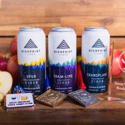 Three cans of Highpoint Cider positioned next to awards and an apple.