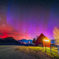 Pink, orange and red northern lights dance in the sky above the Sun Valley barn at night.