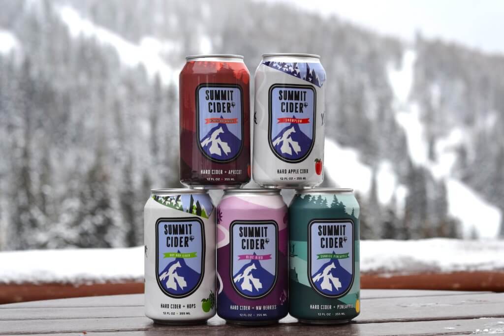 Five Summit Cider cans stacked in a pyramid with a snowy mountain in the background.