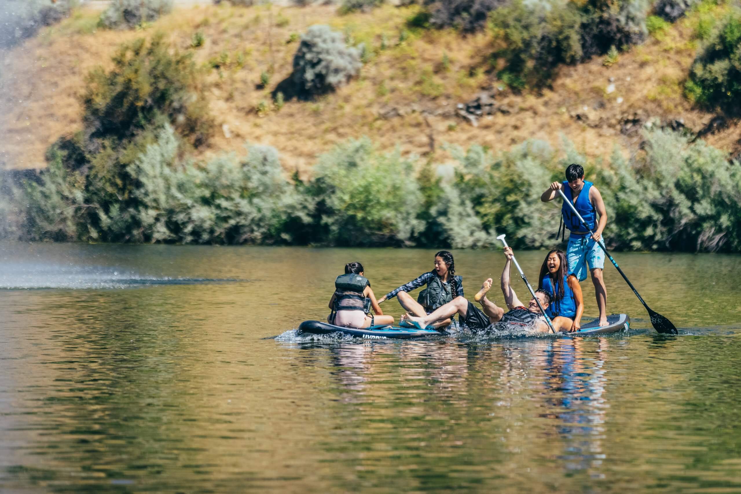 A family sitting on and paddling standup paddleboards at Sandy Point Beach in Lucky Peak State Park.