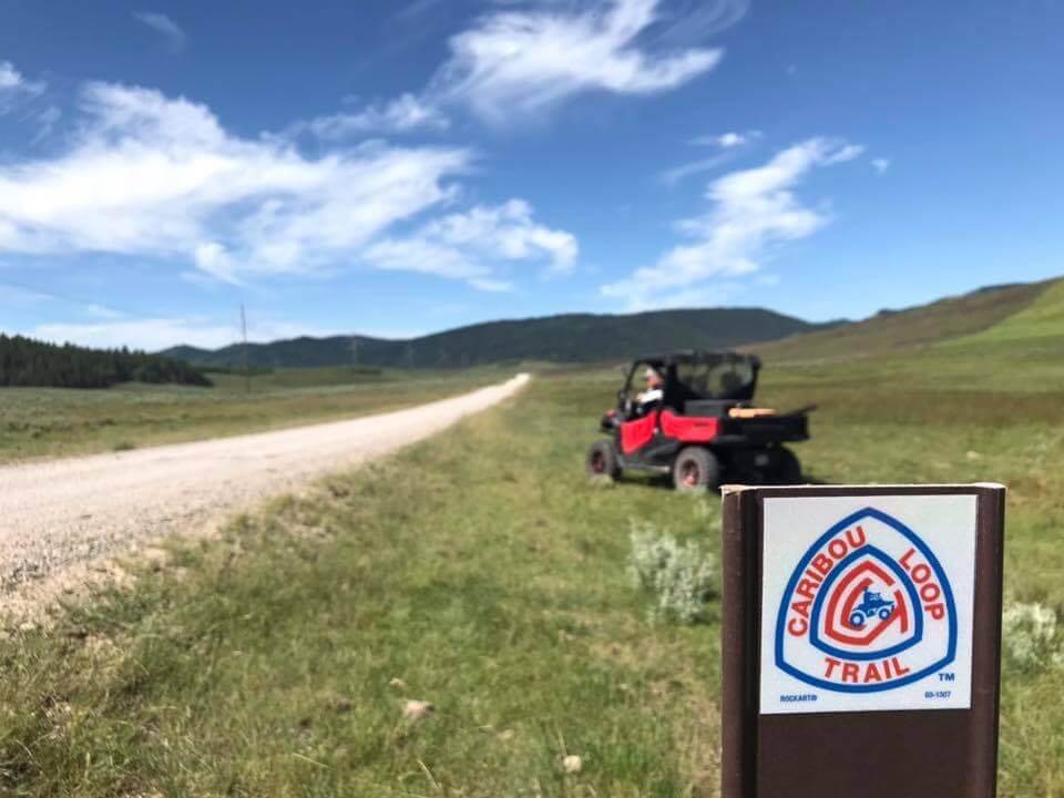 A red ATV sits ahead of a Caribou Loop Trail marker along the trail under a blue sky.