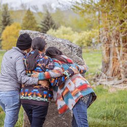 Three women with their arms around each other, standing in front of the Sacajawea Birthplace Monument.