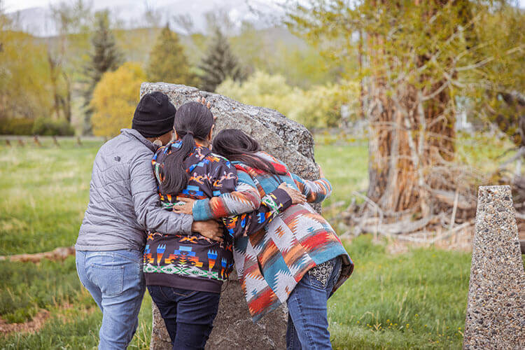 Three women with their arms around each other, standing in front of the Sacajawea Birthplace Monument.