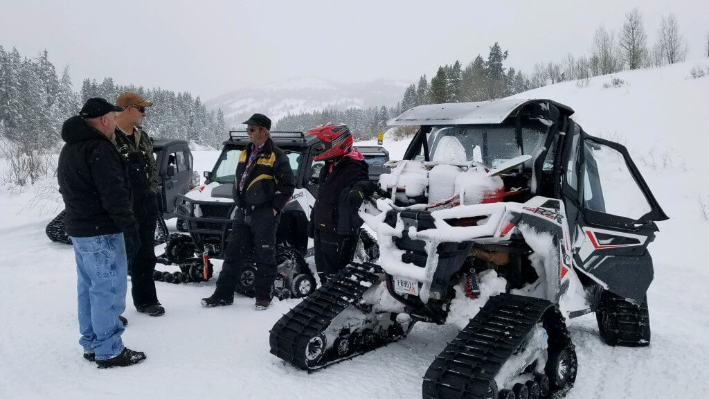 Four people talk in front of three ATVs geared up for winter riding at McCoy Creek. 