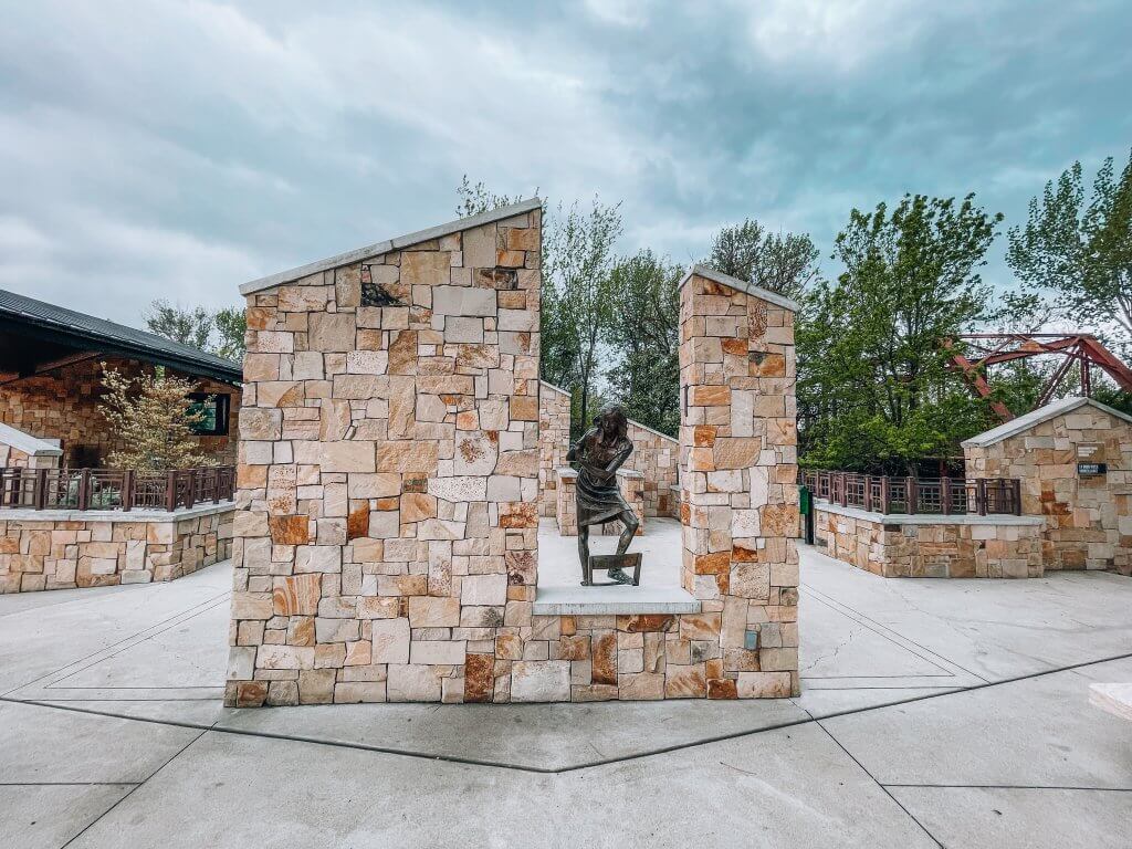 A statue of Anne Frank surrounded by brick walls on two sides on display at the Anne Frank Human Rights Memorial.