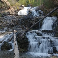 Water runs down three different rock faces creating a multi-tiered waterfall.