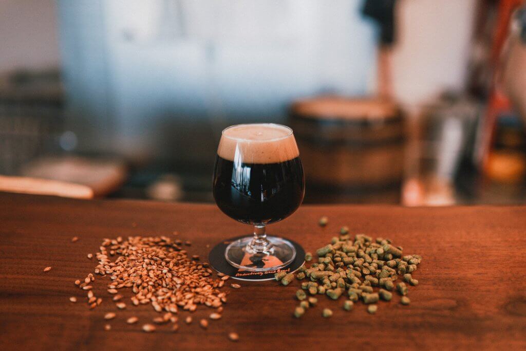 Dark beer in tulip glass with brewing grains.